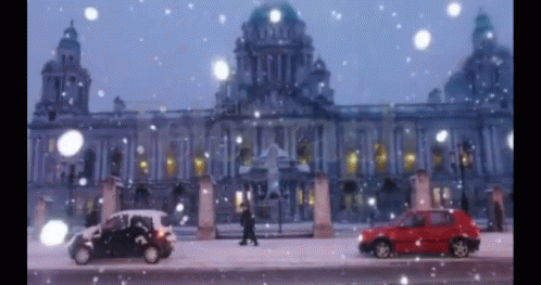 A Red Car Is Parked In Front Of A Building In The Snow GIF