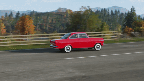A Red Car With White Tires Is Driving Down A Road With Mountains In The Background GIF