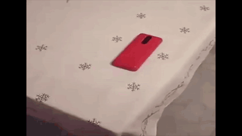 A Red Cell Phone Is Sitting On A White Surface Next To Snowflakes . GIF