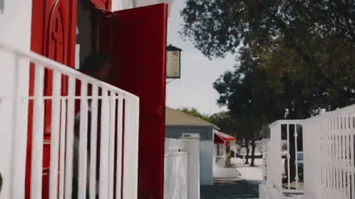 A Red Door With A White Railing Is Open To A White House GIF