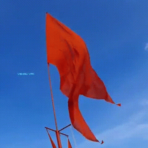 A Red Flag Is Flying In The Wind In Front Of A Blue Sky . GIF