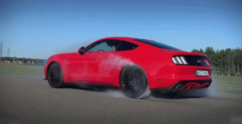 a red ford mustang is driving down a road with smoke coming out of it
