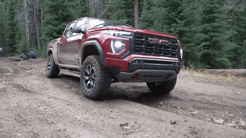 A Red Gmc Truck Is Parked On A Dirt Road In The Woods . GIF
