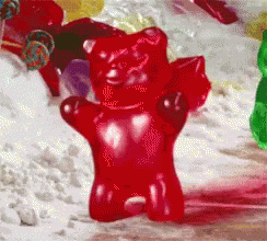A Red Gummy Bear Is Sitting On A Table With Other Gummy Bears GIF