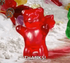 A Red Gummy Bear Is Standing In Front Of A Pile Of Other Gummy Bears . GIF