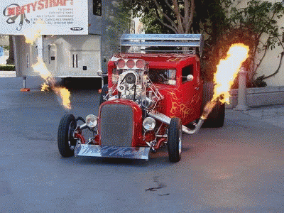 A Red Hot Rod With Flames Coming Out Of It Is Driving Down A Street GIF
