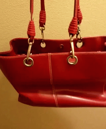 A Red Leather Purse With Two Handles Is Hanging From A Wall GIF