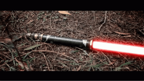 A Red Light Saber Is Laying On The Ground In The Dirt GIF