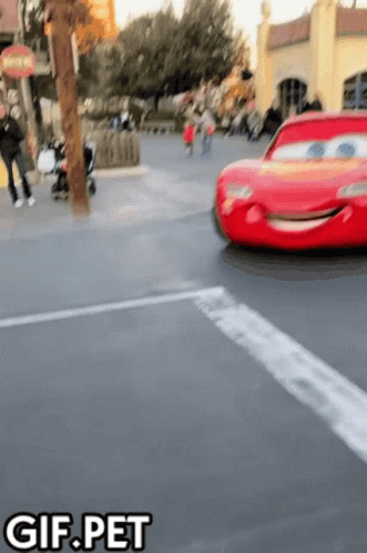 A Red Lightning Mcqueen Car Is Driving Down A Street With The Words Gif.pet Below It GIF