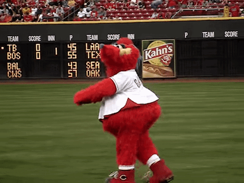 A Red Mascot On A Baseball Field With A Kahn 'S Ad In The Background GIF