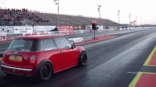 A Red Mini Cooper Is Driving Down A Race Track With A Lucas Oil Sign Behind It GIF