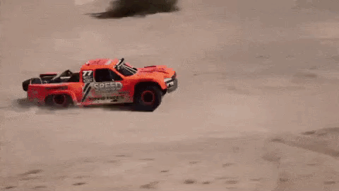 A Red Rc Truck Is Flying Through The Air On A Dirt Road . GIF