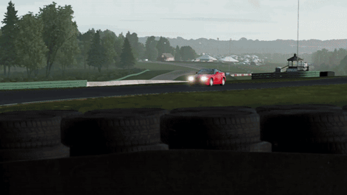 A Red Sports Car Is Driving Down A Track With Tires In The Foreground GIF