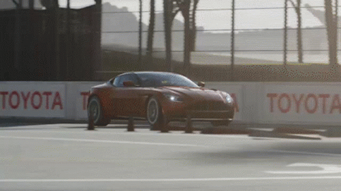 A Red Sports Car Is Driving On A Race Track With Toyota Signs Along The Side GIF