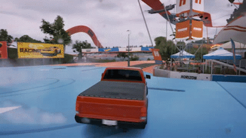 A Red Truck Is Driving On A Blue Track With A Horizon Sign In The Background GIF