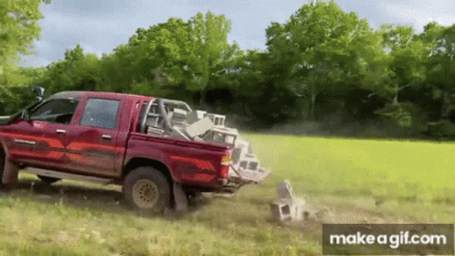 A Red Truck Is Driving Through A Grassy Field With A Pile Of Bricks In The Back . GIF