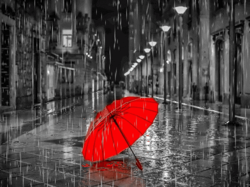 A Red Umbrella Is Sitting In The Rain On A City Street GIF
