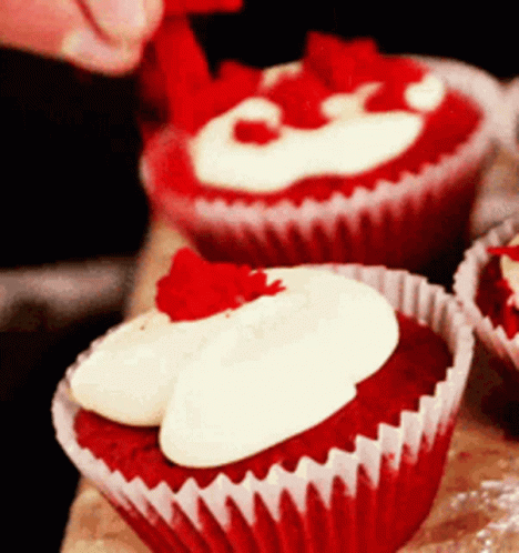 A Red Velvet Cupcake With White Frosting And A Red Strawberry On Top GIF