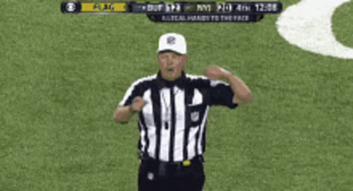 A Referee Giving A Signal On A Field With A Scoreboard Behind Him GIF