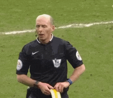 A Referee Is Standing On A Soccer Field Holding A Yellow Flag . GIF
