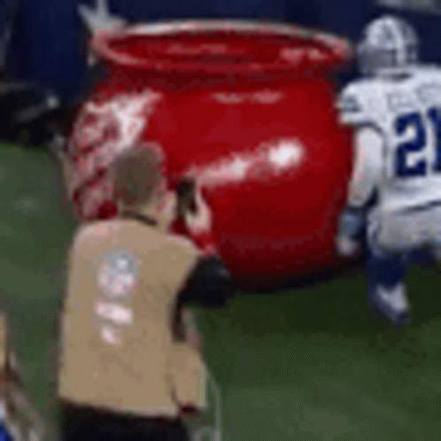 A Referee Is Taking A Picture Of A Football Player And A Large Red Pot On The Field . GIF