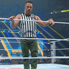 A Referee Stands In The Middle Of A Wrestling Ring With A Wrestlemania Sign In The Background GIF