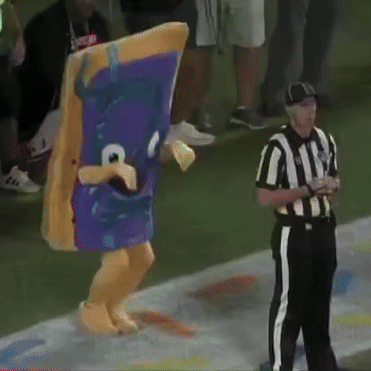 A Referee Stands Next To A Mascot Wearing A Purple Costume GIF