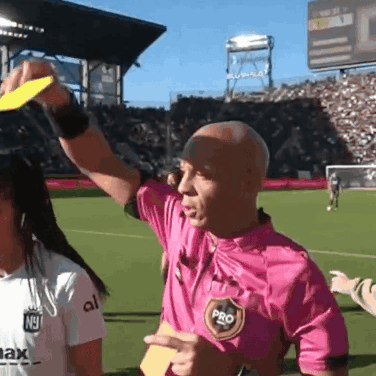 A Referee Wearing A Pink Shirt With The Word Pro On It Holds Up A Yellow Card GIF