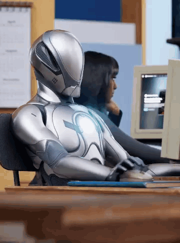 A Robot Is Sitting At A Desk Using A Computer GIF