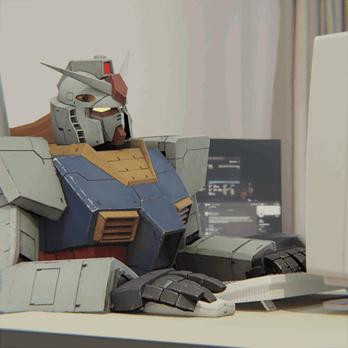 A Robot Sits At A Desk In Front Of A Computer Screen GIF