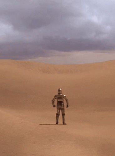 A Robot Stands In The Middle Of A Desert With His Hands On His Hips GIF