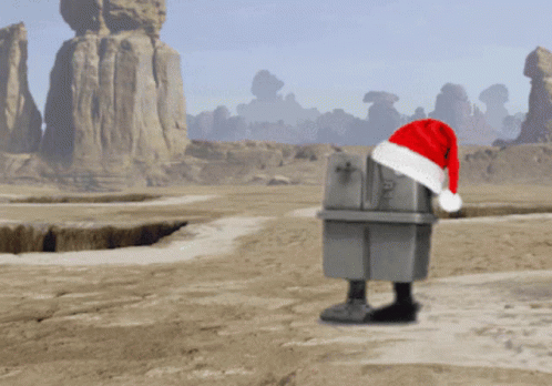 A Robot Wearing A Santa Hat Stands In A Desert GIF