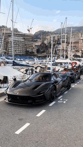 A Row Of Black Sports Cars Are Parked On The Side Of The Road Near A Marina GIF