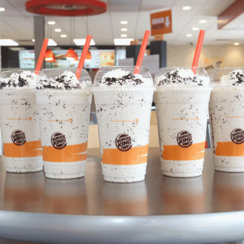 A Row Of Burger King Milkshakes With Straws On A Table GIF