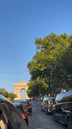 A Row Of Cars Are Parked On A Street In Front Of A Large Archway GIF