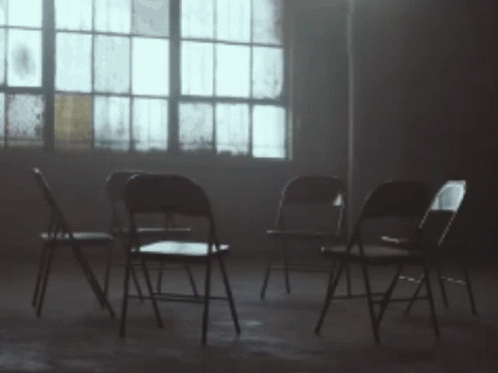 A Row Of Folding Chairs In A Dark Room With A Window In The Background GIF
