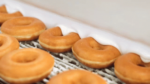A Row Of Glazed Donuts With White Frosting On A Conveyor Belt GIF