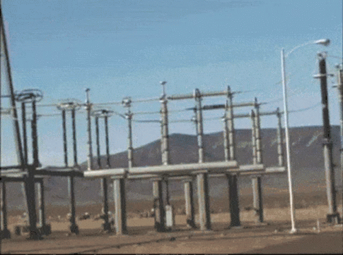 A Row Of Power Lines Are Lined Up In A Field With Mountains In The Background GIF