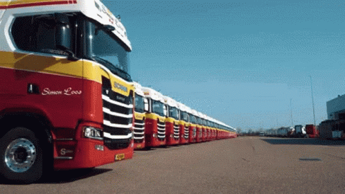 A Row Of Red And Yellow Scania Trucks Are Parked In A Lot GIF