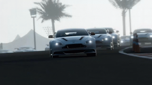 A Row Of Sports Cars Are Driving Down A Road With Palm Trees In The Background GIF
