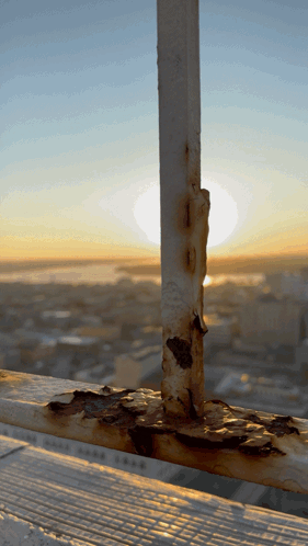 A Rusty Railing With A City In The Background At Sunset GIF