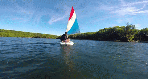 a sailboat with a red white and blue sail is floating on the water