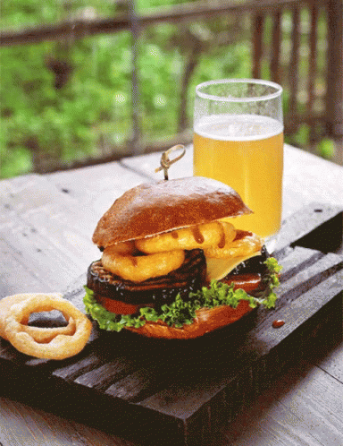 A Sandwich With Onion Rings And A Glass Of Beer On A Wooden Table GIF