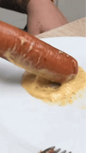 A Sausage Is Being Dipped In A Yellow Sauce On A White Plate With A Fork . GIF