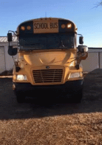 A School Bus Is Parked In A Dirt Lot GIF