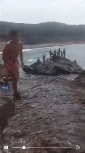 A Screenshot Of A Video Of People On A Rocky Beach With The Time Of 0:01 GIF