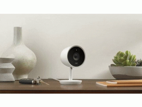 A Security Camera Is Sitting On Top Of A Wooden Table Next To A Vase And Keys . GIF