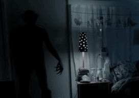 A Shadow Of A Person Standing In A Dark Room With A Lamp GIF