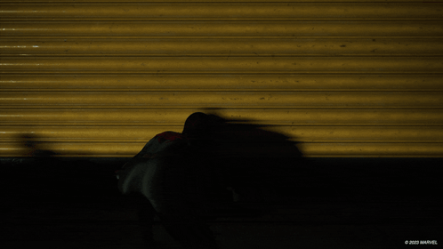 A Shadow Of A Spider Man Is Cast On A Yellow Wall With The Marvel Logo In The Corner GIF