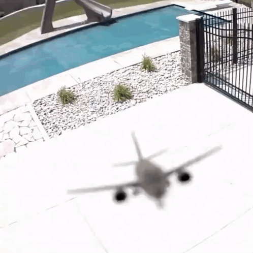 A Shadow Of An Airplane Is Cast On The Ground Near A Swimming Pool GIF